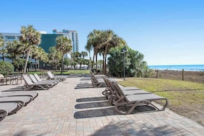 A sunlit outdoor seating area with lounge chairs and a view of the ocean. - The Patricia Grand 1002 (Myrtle Beach)