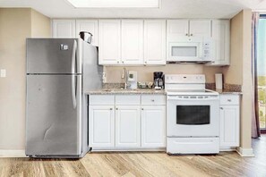 A kitchen with white cabinets, a stainless steel refrigerator, a microwave, and a stove. - The Patricia Grand 1002 (Myrtle Beach)