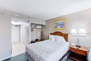 Ein Hotelzimmer mit Bett, Nachttischlampen, einem Nachttisch, einem Kleiderhaken und einem Bild an der Wand.