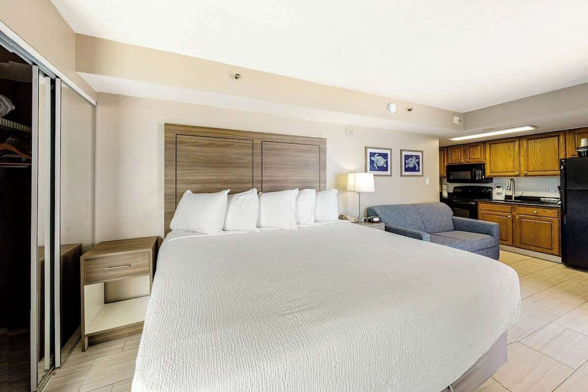 Una camera d'albergo con un letto grande, un comodino, una sedia, un armadio e un angolo cottura.