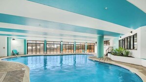 Una piscina interna con pareti di vetro trasparente, pavimento piastrellato e soffitto blu.