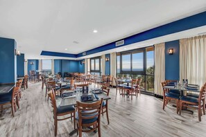 A spacious dining area with multiple tables and chairs, large windows, and a view of the outdoors. - The Patricia Grand 1102 (Myrtle Beach)
