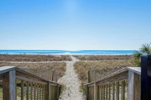 Ein hölzerner Weg führt zu einem Strand mit freiem Blick auf das Meer.