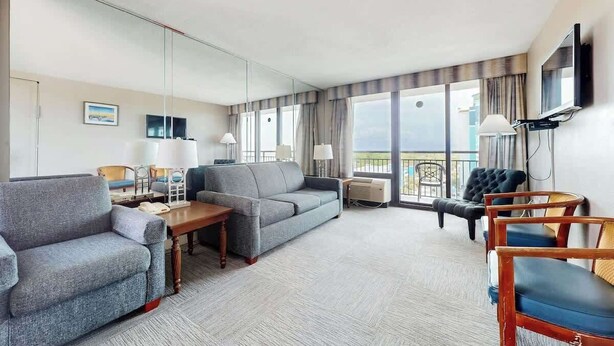 Habitación de hotel con sofá, sillones, una mesa, televisor y balcón con vistas.