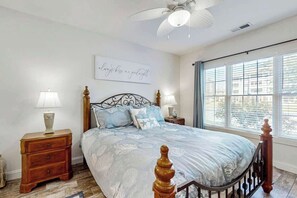 A bedroom with a bed, two bedside tables, a wall-mounted light fixture, and a window with blinds. - Magnolia Pointe Unit 103 (Myrtle Beach)