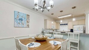 A dining area with a wooden table, white chairs, and a chandelier. - Magnolia Pointe Unit 103 (Myrtle Beach)