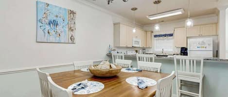 Comedor con mesa de madera, sillas blancas y una lámpara de araña.