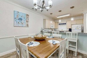A dining area with a wooden table, white chairs, and a chandelier. - Magnolia Pointe Unit 103 (Myrtle Beach)