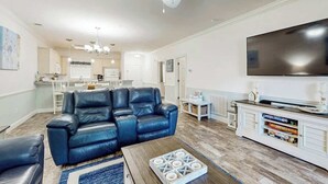 A living room with a black leather sofa, a wooden coffee table, and a flat-screen TV on a white cabinet. - Magnolia Pointe Unit 103 (Myrtle Beach)