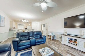 A living room with a black leather sofa, a wooden coffee table, and a flat-screen TV on a white cabinet. - Magnolia Pointe Unit 103 (Myrtle Beach)
