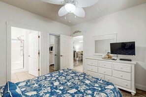 Un dormitorio con cama, televisión, cómoda y una puerta abierta que da a un baño.