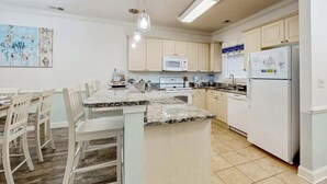 A kitchen with white cabinets, a granite countertop island, a microwave, and a refrigerator. - Magnolia Pointe Unit 103 (Myrtle Beach)