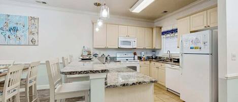 A kitchen with white cabinets, a granite countertop island, a microwave, and a refrigerator.