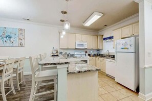 A kitchen with white cabinets, a granite countertop island, a microwave, and a refrigerator. - Magnolia Pointe Unit 103 (Myrtle Beach)