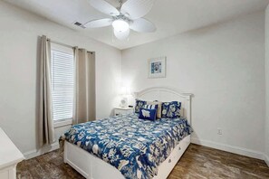 A bedroom with a bed, a ceiling fan, a nightstand, and a window with curtains. - Magnolia Pointe Unit 103 (Myrtle Beach)