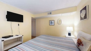 Ein Hotelzimmer mit einem Bett, einem flachbildfernseher an der Wand, einem Nachttisch mit Lampe sowie einem gerahmten Bild.