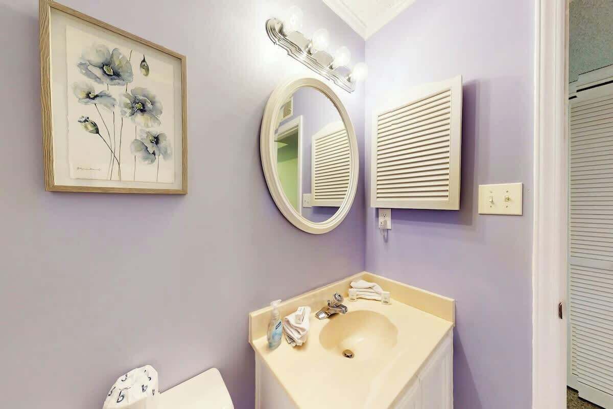 A bathroom with a sink, mirror, framed artwork, and a lighted vanity mirror.