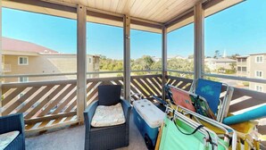 Ein überdachter Balkon mit einem Korbstuhl, einer kleinen Couch und einer Kühlbox.