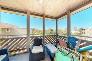 A covered balcony with a wicker chair, a small sofa, and a cooler. - Waipani Unit C-15 Condo (North Myrtle Beach)