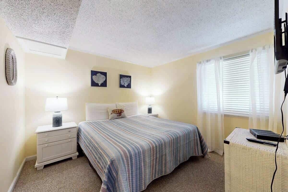 A bedroom with a bed, bedside tables, a lamp, a wall clock, and a window with curtains.