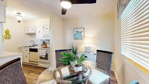Eine moderne Küche mit weißen Schränken, ein Essbereich mit einem Glastisch und einem Deckenventilator.