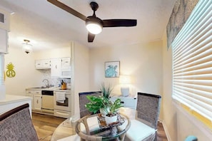 A modern kitchen with white cabinetry, a dining area with a glass table, and a ceiling fan. - Waipani Unit C-15 Condo (North Myrtle Beach)