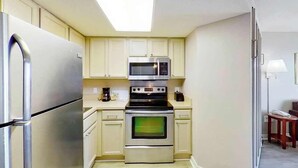 Eine kleine Küche mit Kühlschrank, Mikrowelle, Backofen und Kaffeemaschine.