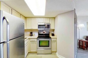 Eine kleine Küche mit Kühlschrank, Mikrowelle, Backofen und Kaffeemaschine.