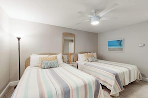 Une chambre d’hôtel avec deux lits, un ventilateur de plafond, une table de chevet, une lampe, un miroir et un tableau au mur.
