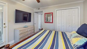 A bedroom with a bed, a ceiling fan, a television, a dresser, and a door. - Pawleys Island Unit #2 (Pawleys Island)