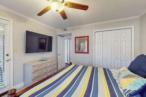 Ein Schlafzimmer mit Bett, Deckenventilator, Fernseher, Kommode und Tür.