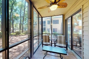 Eine überdachte Terrasse mit Deckenventilator, großen Fenstern und einer Sitzbank.
