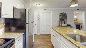 A kitchen with white cabinets, a stainless steel refrigerator, a granite countertop, and a pendant light. - Pawleys Island Unit #2 (Pawleys Island)