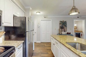 Eine Küche mit weißen Schränken, einem Edelstahl-Kühlschrank, einer Granit-Arbeitsplatte und einer Pendelleuchte.