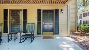 A covered porch with a lattice ceiling, a door marked with the number 2, and a small table and chair. - Pawleys Island Unit #2 (Pawleys Island)