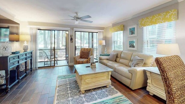 A living room with a sofa, coffee table, and armchairs, a dining area with a table and chairs, and a large window with blinds. - Pawleys Island Unit #2 (Pawleys Island)