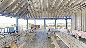 An outdoor covered deck with picnic tables and chairs, overlooking a body of water. - Dunes Pointe Unit C-14 (Myrtle Beach)