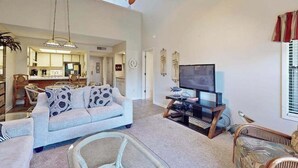 A spacious living room with a sofa, a television, and a ceiling fan. - Dunes Pointe Unit C-14 (Myrtle Beach)