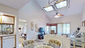 A living room with a television, a sofa, and a dining area with a table and chairs. - Dunes Pointe Unit C-14 (Myrtle Beach)