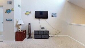 A room with a flat-screen TV mounted on the wall, a wooden dresser, a lamp, and a small cabinet. - Dunes Pointe Unit C-14 (Myrtle Beach)