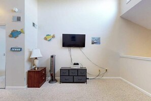 Ein Zimmer mit flachbildfernseher an der Wand, einem Holzkoffer, einer Lampe und einem kleinen Schrank.