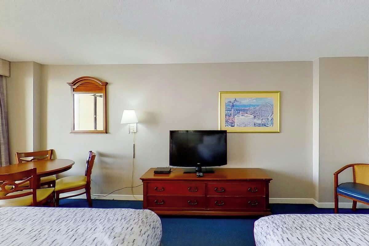 Ein Hotelzimmer mit zwei Betten, einem Fernseher auf einer Holzkommode, einem Bild an der Wand und einem Spiegel über der Kommode.