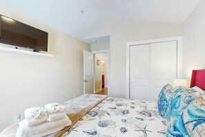 Una camera d'albergo con un letto, una televisione fissata al muro, una porta che dà su un'altra stanza e un corridoio.