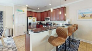 A modern kitchen with dark wood cabinets, a stainless steel refrigerator, and a central island with seating. - Corals and Oars Retreat (Myrtle Beach)