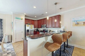 A modern kitchen with dark wood cabinets, a stainless steel refrigerator, and a central island with seating. - Corals and Oars Retreat (Myrtle Beach)