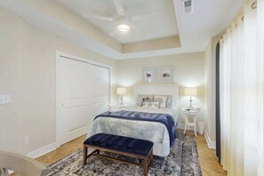 A bedroom with a bed, bedside tables, a bench, and a ceiling fan. - Corals and Oars Retreat (Myrtle Beach)