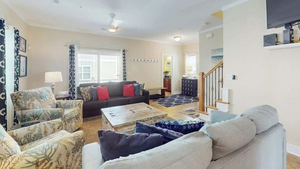 A living room with a sofa, armchairs, a coffee table, and a staircase leading to another level. - Corals and Oars Retreat (Myrtle Beach)