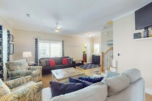 A living room with a sofa, armchairs, a coffee table, and a staircase leading to another level. - Corals and Oars Retreat (Myrtle Beach)