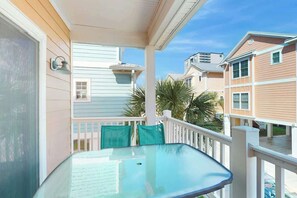 A glass-top table on a balcony with a white railing and a view of neighboring houses. - Corals and Oars Retreat (Myrtle Beach)