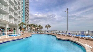 Uma piscina com espreguiçadeiras, um edifício com varandas e vista para o oceano.